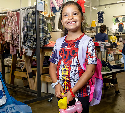 Voices for Children partnered with Old Navy Back for the annual Back to School Event.  A female child has a new backpack and a balloon animal. 